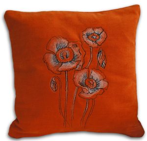 Oranssi pehmeäpintainen tyyny, jossa brodeerattu keveän läpikuultava Unikot-kuvio.