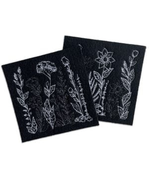Mustat huovasta valmistetut lasinaluset, joissa konekirjottuja kukkakuvioita valkoisella ja tumman harmaalla.