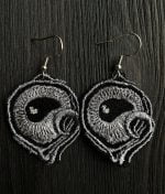 On a black surface, Ikiiurso-earrings handcrafted from viscose and metallic thread with black eye in the middle surrounded by gray "tentacles".
