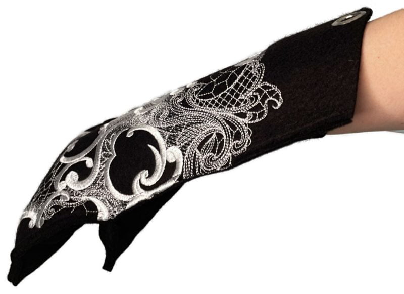 Musta villahuovasta käsityönä valmistettu pääkallokuvioinen patakinnas naisen kädessä.