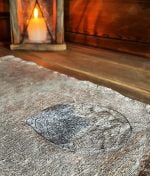 Close-up of a linen cloth with gray embroidered leaf on sauna bench. On the background a atmospheric lantern with lit candle.