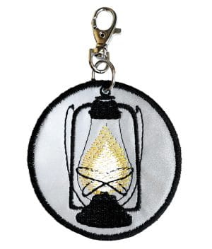 Handcrafted round reflective pendant. The handdrawn Hurricane lantern is machine embroidered with black rayon thread.