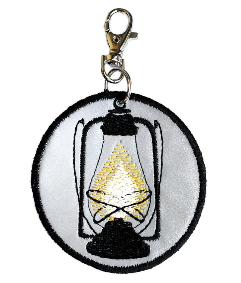 Handcrafted round reflective pendant. The handdrawn Hurricane lantern is machine embroidered with black rayon thread.