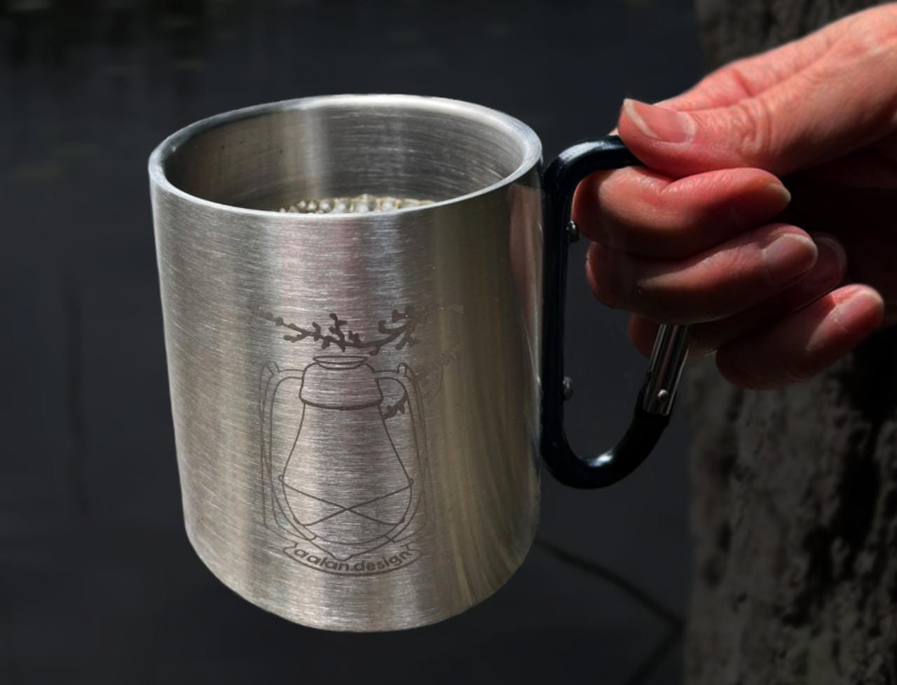 Kippis Tummataustainen kuva, jossa naisen käsi kohottaa maljan rosterisella AAlan Designin Lyhty-retkimukilla, jossa kahvia.